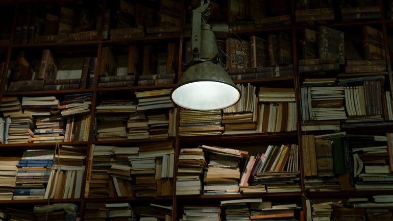 Тёплая настольная лампа освещает раскрытые книги в уютном уголке для чтения