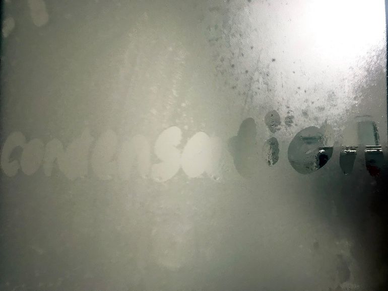 Слово condensation, написанное пальцем на запотевшем стекле с каплями влаги