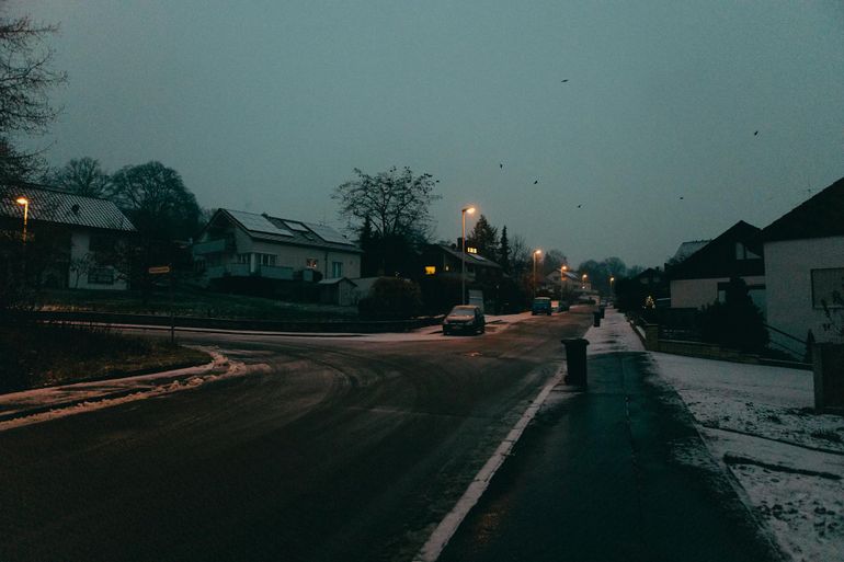 Заснеженная пригородная улица в сумерках с тусклыми фонарями