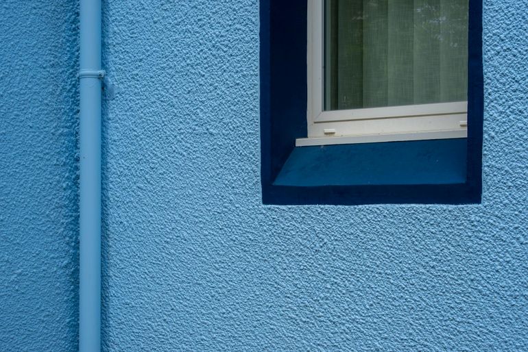 Окно в стене с оштукатуренным откосом и водосточной трубой снаружи фасада