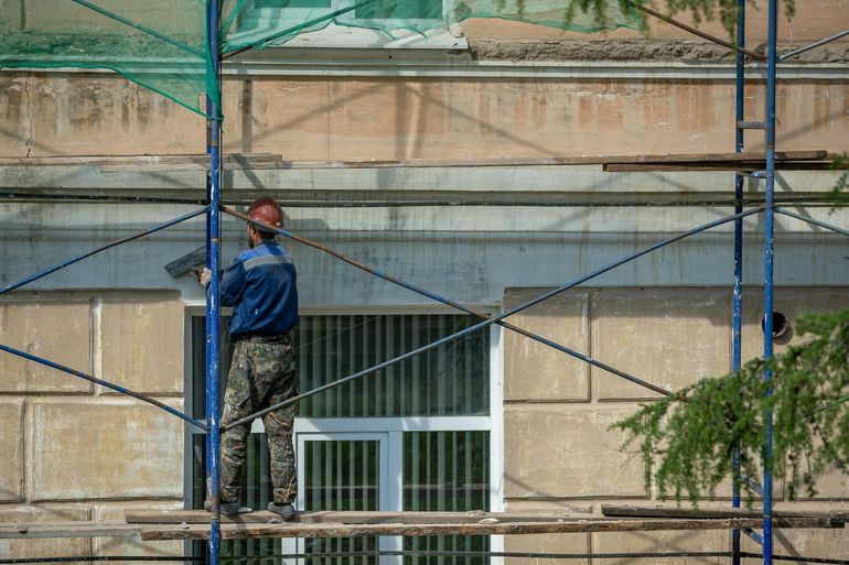 Рабочий в каске на лесах ремонтирует фасад здания снаружи