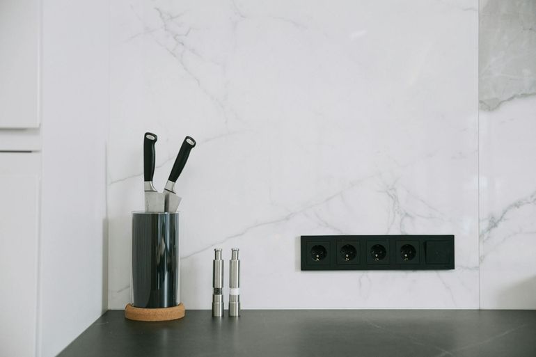 Розетки над кухонным фартуком из мрамора рядом с подставкой для ножей