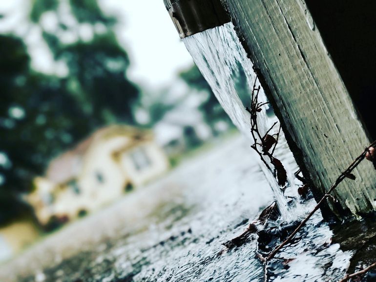 Поток дождевой воды льётся из водосточной трубы во время ливня