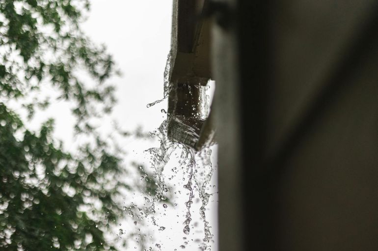 Поток дождевой воды стекает из водосточного жёлоба во время сильного ливня
