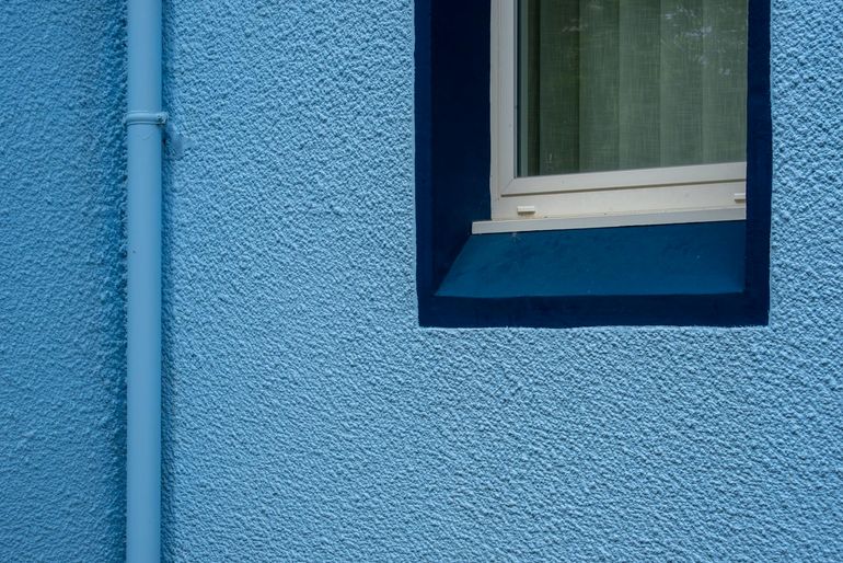 Окно в стене с оштукатуренным откосом и водосточной трубой снаружи фасада