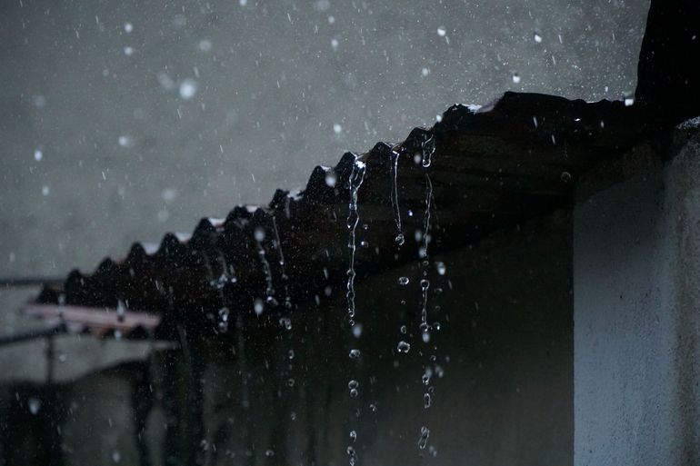 Дождевая вода стекает каскадом с края металлической кровли