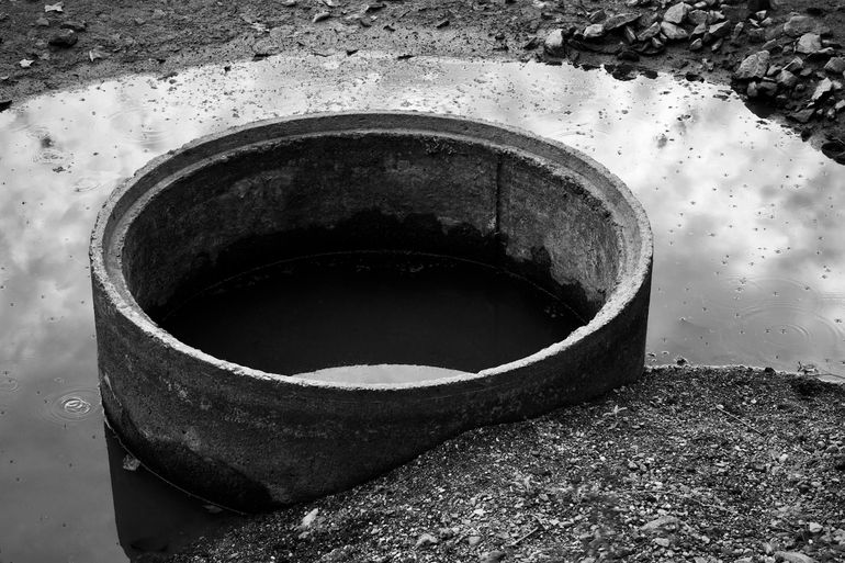 Круглое бетонное кольцо колодца в луже воды на участке