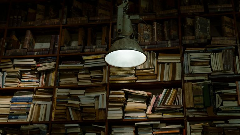 Тёплая настольная лампа освещает раскрытые книги в уютном уголке для чтения