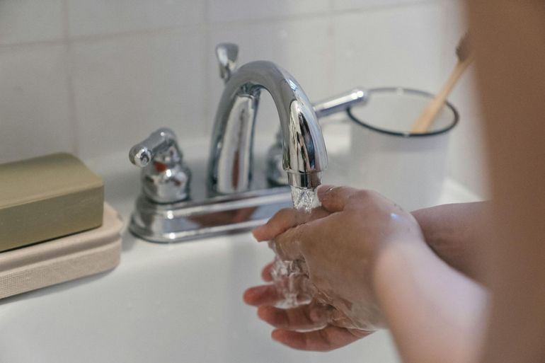 Руки под струёй проточной воды у крана для промывания