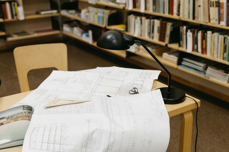 Архитектурные чертежи и документы на рабочем столе под настольной лампой