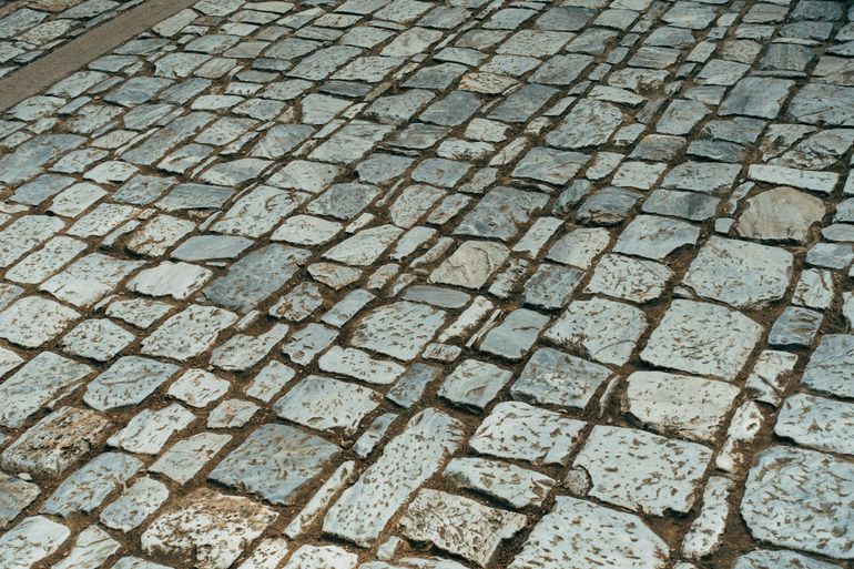Старая брусчатка из гранита уложена плотным узором на песчаном основании дорожки