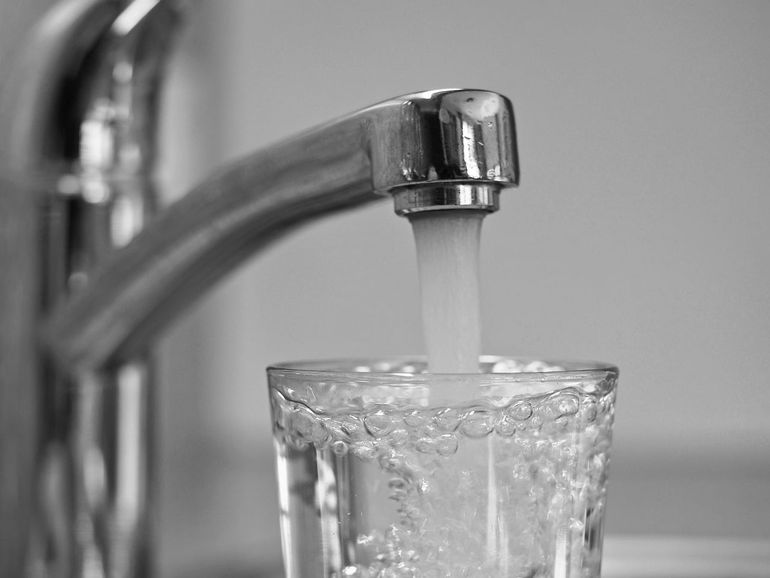 Струя воды из крана наливается в подставленный стакан для проверки