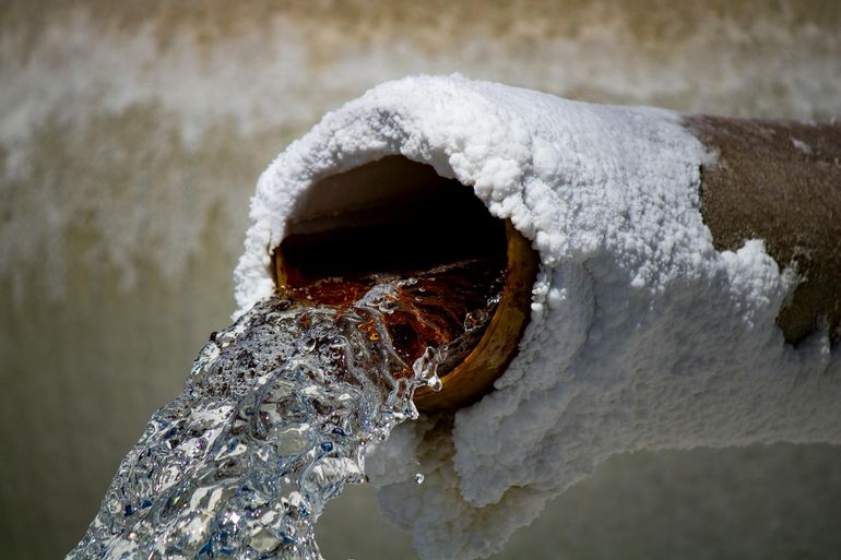 Поток воды из ржавой трубы с солевыми отложениями и видимой взвесью