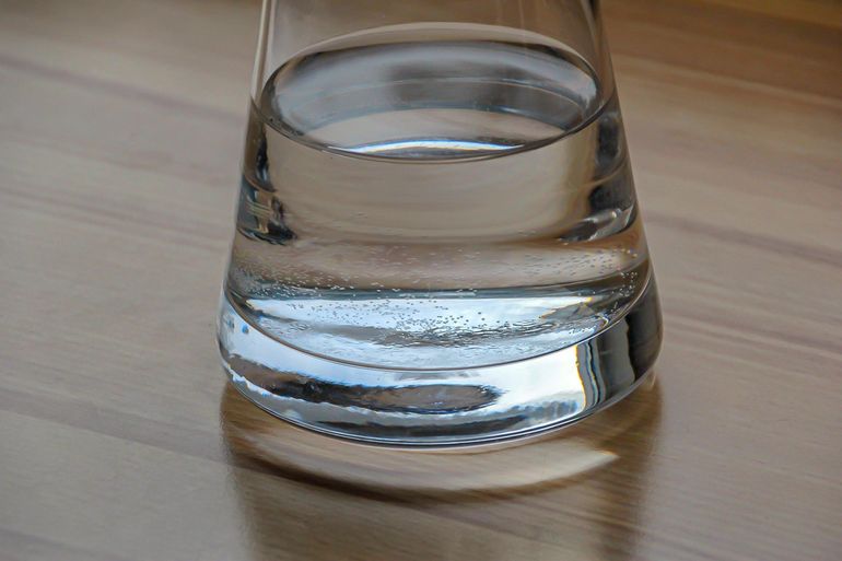 Наполнение стакана чистой водой из кухонного крана над мойкой