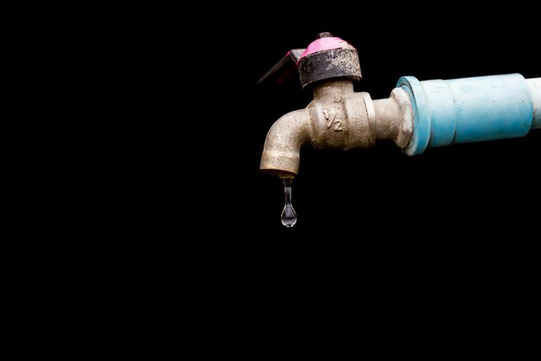 Капля воды на металлическом смесителе крупным планом на тёмном фоне