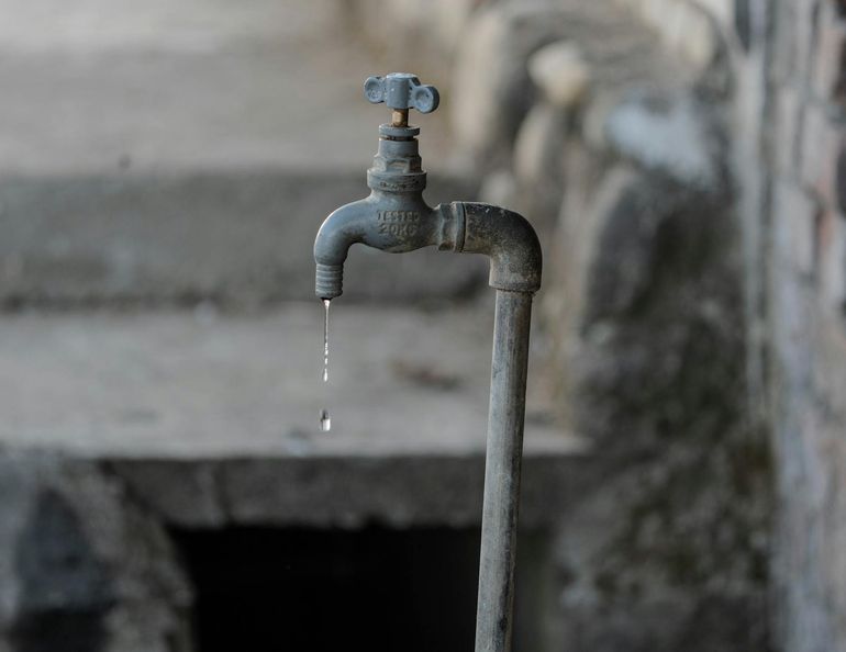 Старый уличный кран с каплей воды на фоне грубой стены
