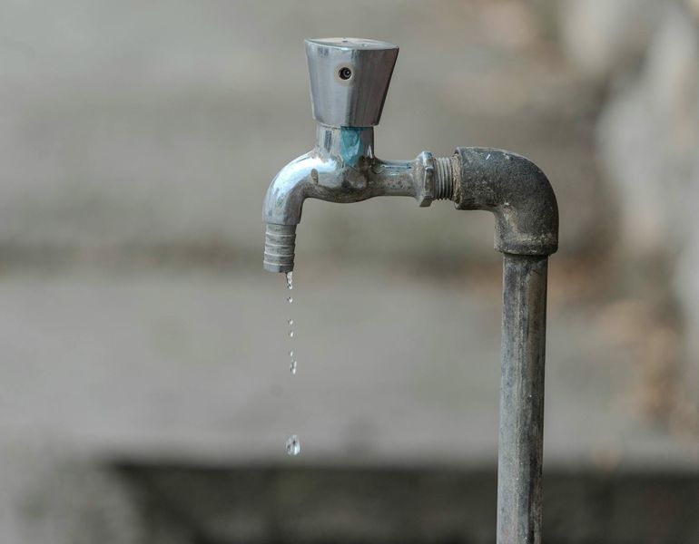 Капля воды срывается с металлического крана крупным планом