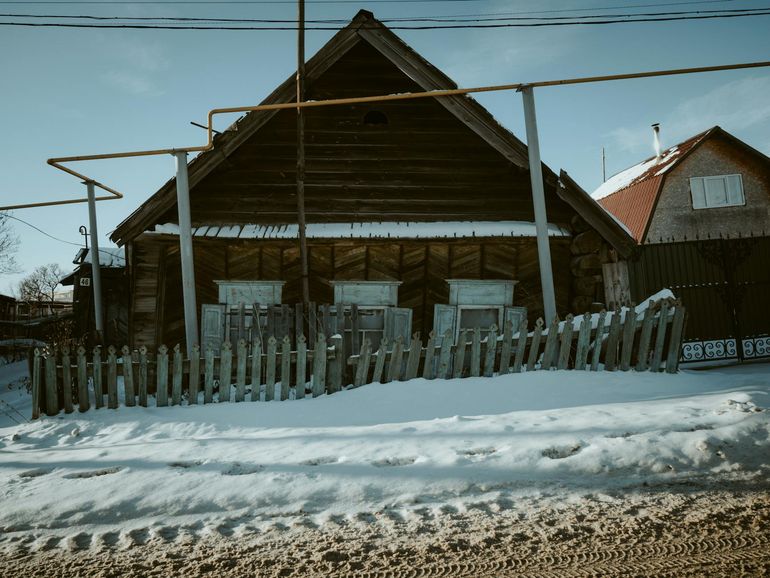 Деревянный загородный дом зимой с заснеженным забором вдали от магистралей