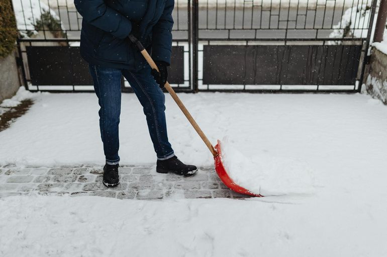Человек чистит лопатой снег с мощёной дорожки зимой