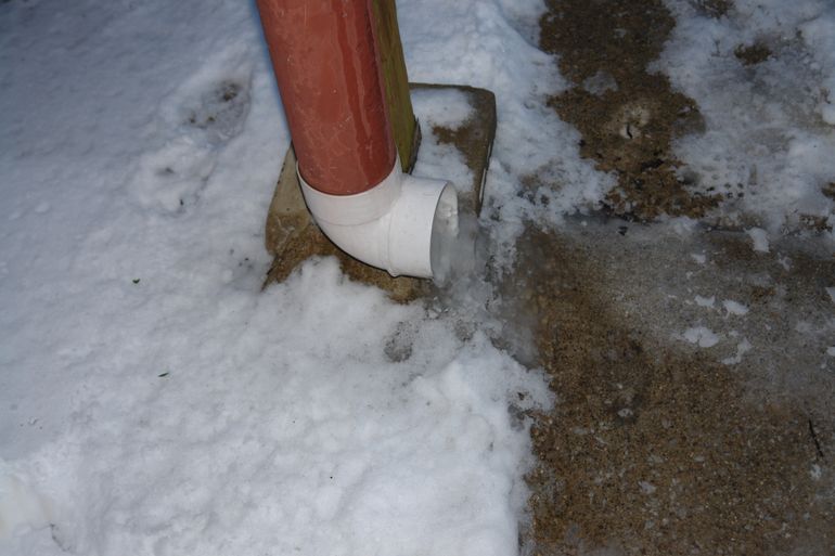 Замёрзшая вода натекла из водосточной трубы на тротуар зимой