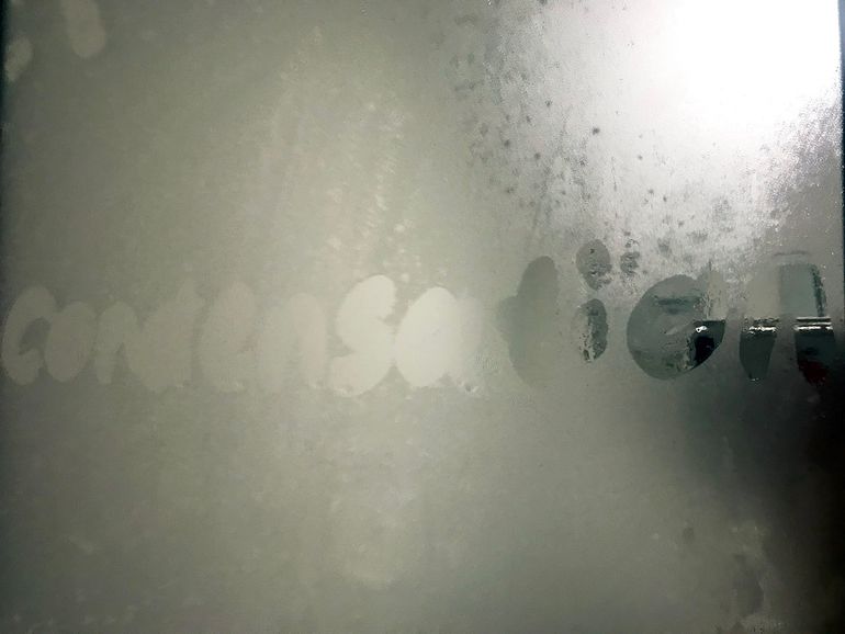 Слово condensation, написанное пальцем на запотевшем стекле с каплями влаги