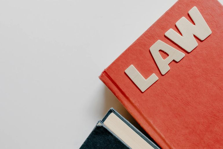 Юридический учебник в красной обложке рядом с тёмной книгой на белом фоне